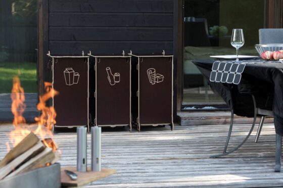 Eco-friendly outdoor waste sorting bins made from sustainable materials, placed on a wooden terrace near a home, symbolizing modern sustainable living.
