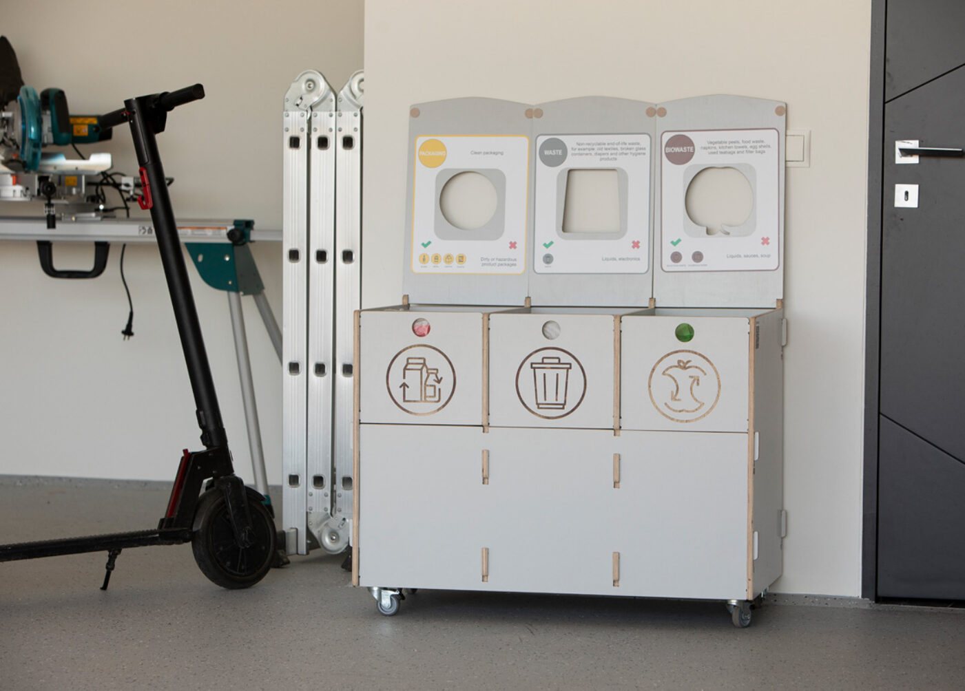 Recycling bins for office supply areas placed near storage shelves to support packaging recycling.