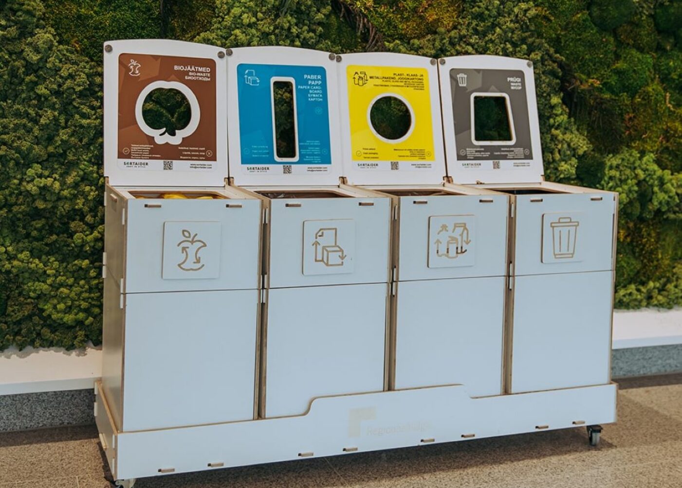 Waste bins with instructional stickers helping children understand waste sorting in a kindergarten classroom.