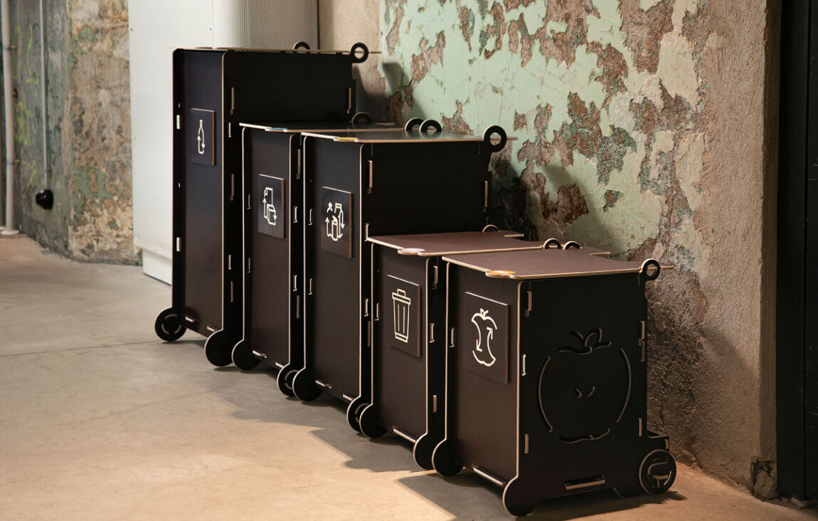 Svarta papperskorgar för kontor med lock och återvinningssymboler, med separata fack för papper, förpackningar, blandat avfall och bioavfall.