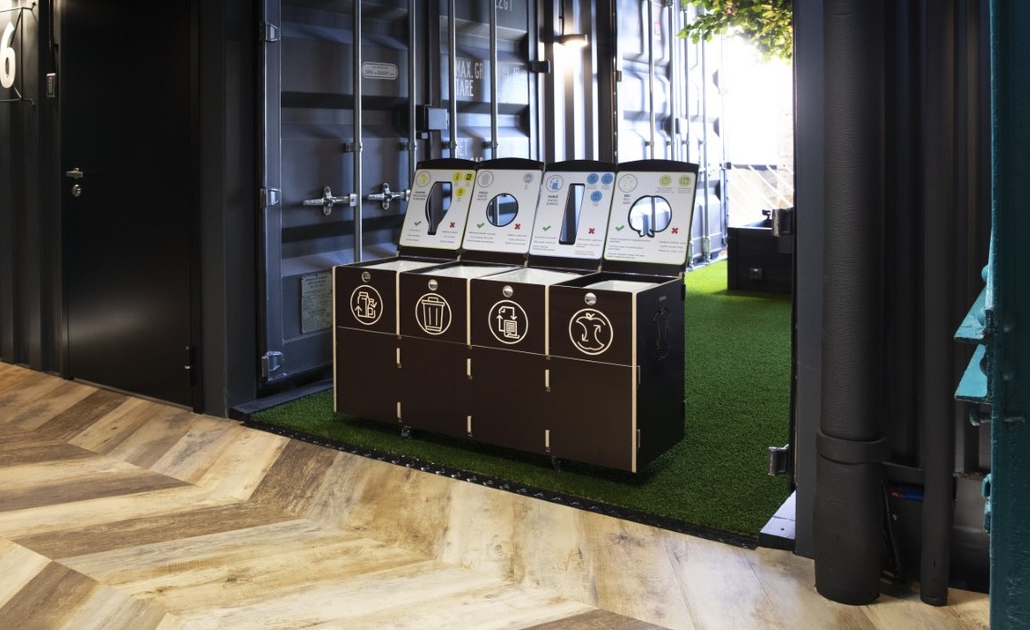 A high-end wooden recycling bin for office environments featuring an open-lid sorting system in a modern shared zone.