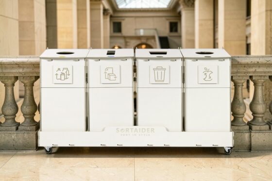 Recycling bins for education systems on a wheeled base, featuring clear waste sorting pictograms, placed in an elegant university campus hallway.