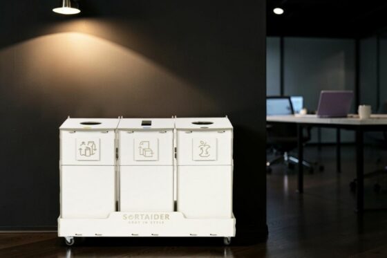 Office recycling bin. Three-compartment birch plywood sorting station on wheels in a modern office.