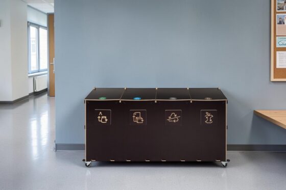 Recycling bin for schools and educational institutions. Four-compartment birch plywood sorting station on wheels in a school corridor.